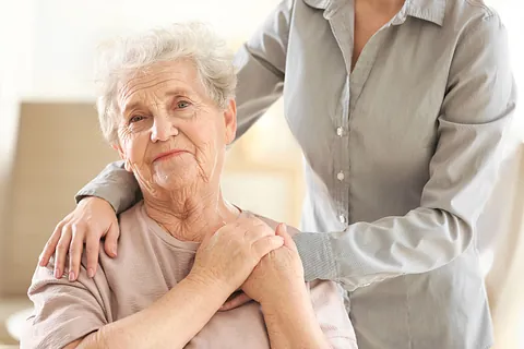 Eine Seniorin, der eine junge Frau die Hände auf die Schultern legt